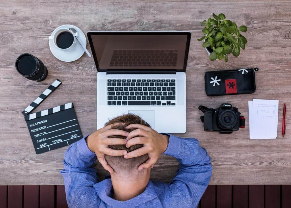 Homem com a mão na cabeça enquanto tem dificuldade de trabalhar em frente ao computador