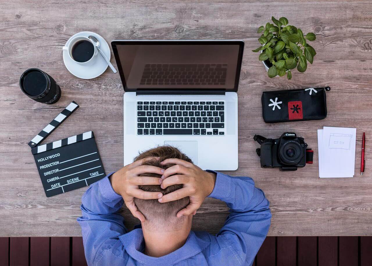 Homem com a mão na cabeça enquanto tem dificuldade de trabalhar em frente ao computador